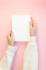 Top view vertical mockup blank paper sheet A4 holds by female hands on pink background. Copy space...