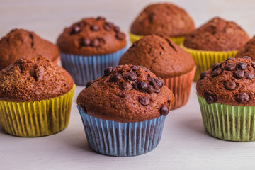 A few chocolate-sprinkled muffins in colored cups on a white wooden surface.