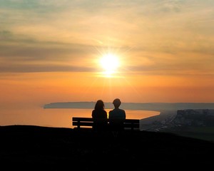 Fototapeta na wymiar Young couple sitting on a bench looking out to sea a the sunset in East Sussex 