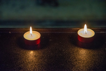 Close up of two votive candles in a church. Candles in the dark with flames on red copper supports. - obrazy, fototapety, plakaty