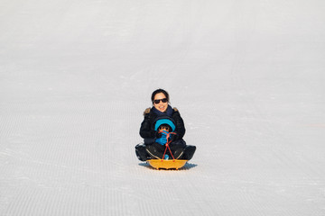 a parent is playing a slide board with son in the winter season at the snow mountain.