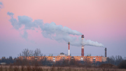 Chimney pipe at sunrise. Environmental Pollution and Global Warming Concept.The chimney pipe emits thick,dark smoke into the atmosphere.Residential building and birds flying near.