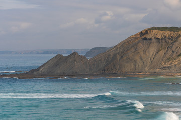 Aljezur beach with waves crashing and sea cliffs on the background