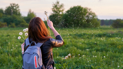 Girl at sunset blowing on dandelions.