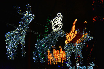 Large golden sleigh of Santa Claus with luminous deer weighing between winter trees in the city park of Dnipro, Ukraine. Bright colorful New Year and Christmas decorations made of diodes, light bulbs.