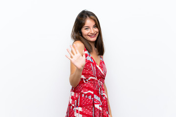 Caucasian girl in red dress over isolated white wall saluting with hand with happy expression