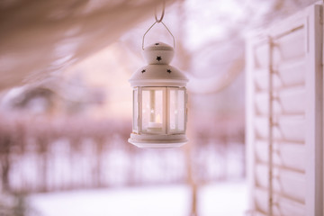 Cozy white lantern on a window with blurred winter landscape seen through the window. © icemanphotos
