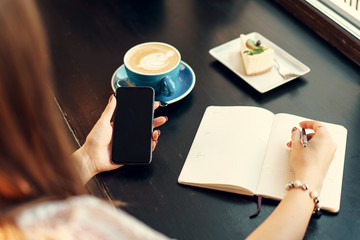 Young business woman sitting at the table in a coffee shop and making notes