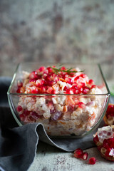 Beautiful meat salad with pomegranate seeds, dressed with mayonnaise and decorated with a sprig of dill on a gray background. Vertical photography