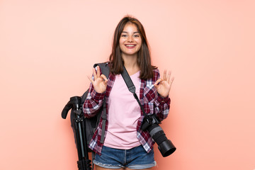 Young photographer girl over isolated pink background showing an ok sign with fingers