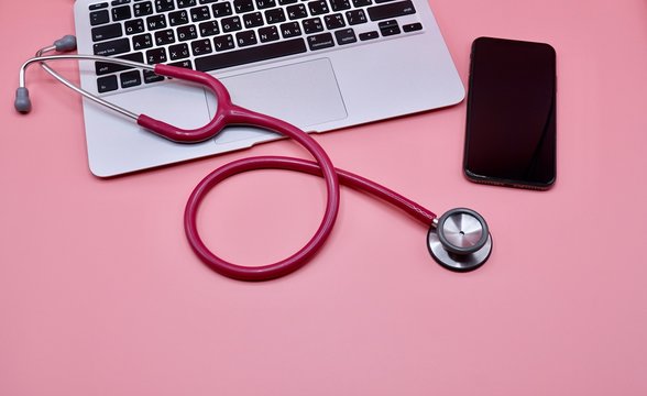 A pink stethoscope with laptop and black smart phone on the pink background