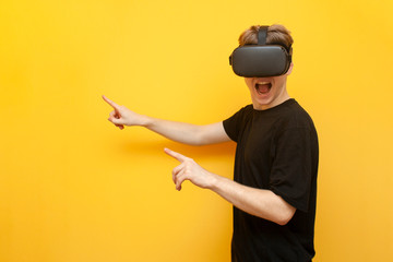 guy a gamer in VR glasses on a yellow background holds a device and points his fingers to a place for text, a man with wireless gadgets for virtual reality