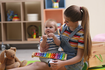 Teen nanny and cute little baby playing with xylophone at home