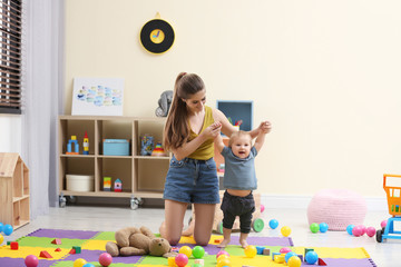 Teen nanny playing with cute little baby at home - obrazy, fototapety, plakaty