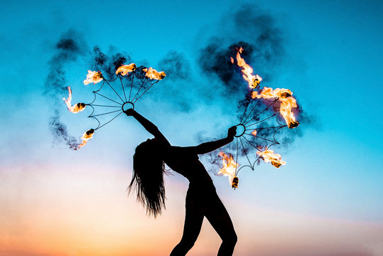 Fire show at sunset. Silhouette of a girl with burning torches