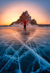 Traveler man wear red clothes and raising arm standing on natural breaking ice in frozen water at sunrise in Lake Baikal, Siberia, Russia.