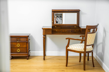 Close-up of chair and wooden table with mirror. White wall.