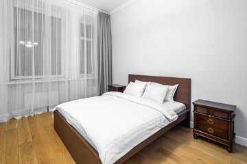 Modern interior in light tones. Bedroom with wooden furniture. White curtain.