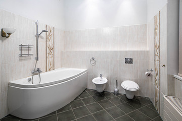 Naklejka na ściany i meble Modern interior of bathroom in light tones with black tile on the floor. Bath, toilet and bidet.