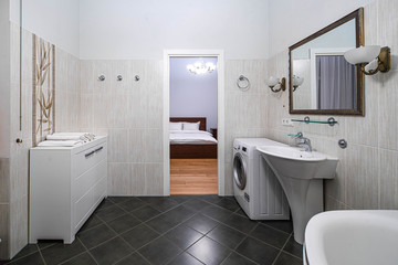 Fototapeta na wymiar Modern interior of bathroom in light tones with black tile on the floor. Opened door. Washing machine.