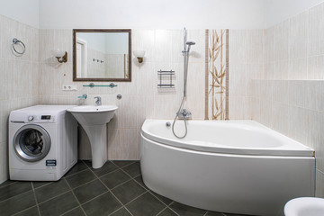 Modern interior of bathroom in light tones with black tile on the floor. Bath, sink, washing machine.