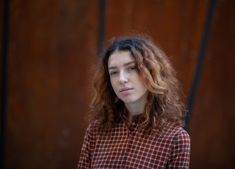 Dreaming young woman with spectacular curly red ginger hair looking at camera posing outdoor in downtown street. Female portrait.