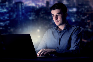 Young handsome businessman working late at night in the office with blue lights in the background