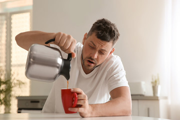Sleepy man pouring coffee into cup at home in morning