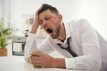 Sleepy man with cup of drink at home in morning