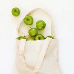 Reusable cotton textile bag with green apples on a white background. The concept of zero waste, green shopping. Square, top view with copy space for text.