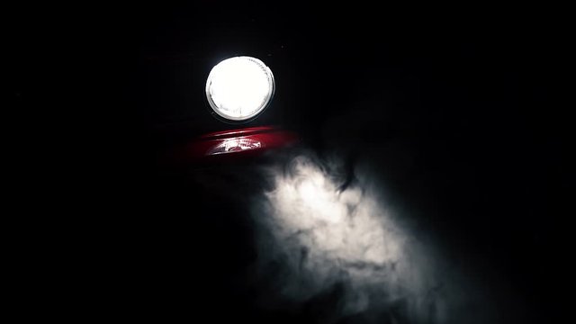 Fog or mist moving in light beam of red car round headlight, slow motion close up