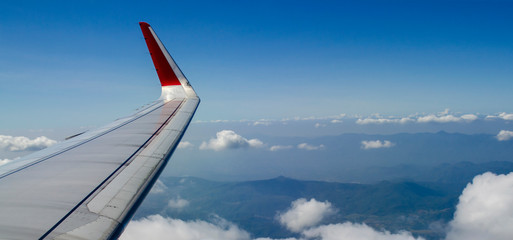 The wings of the plane while in the sky, there are clouds and mountains below.View from plane window while travelling