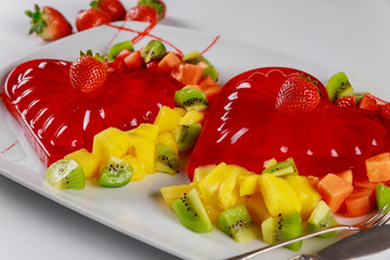 Red gelatin heart shape with chopped fresh fruit on a white background.
