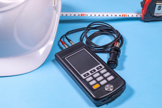 White hardhat, ultrasonic measurement device and a tape-line illustrating non destructive testing procedures (ndt).