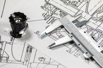 Some pump blueprints on a wooden desk with a magnithing glass and a calipers.