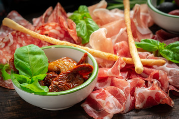 Italian meat appetizers and on a wooden plate. Wine snack Antipasto-salami, prosciutto, slices ham, beef jerky and bread sticks.