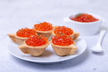 Naklejka na ściany i meble Red caviar (salmon caviar) in tartlets. In the background is a white bowl with caviar. Selective focus, close-up.
