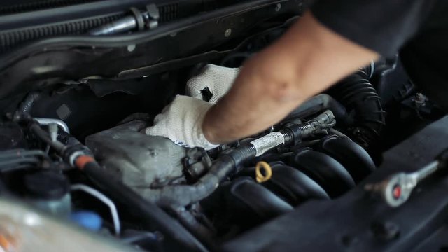 Male auto mechanic changes spark plugs in a car engine