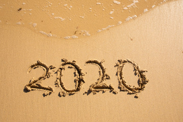 Summer beach holiday 2020 season golden sand - year - decade - new season lettering on the beach with wave and clear blue sea. Numbers 2020 year on the sea shore, message handwritten New Years concept