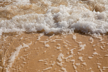 Waves breaking on an empty sand beach and spalsh producing foam - travel holiday vacation summer sun - splashing water - wavy golden yellow sand background - empty space