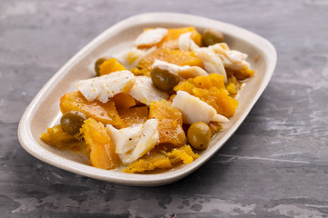 cod fish with sweet potato and olives on dish on ceramic background
