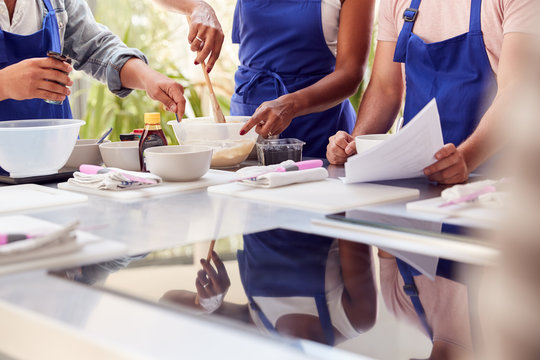Close Up Of Male And Female Adult Students Looking At Recipe In Cookery Class In Kitchen