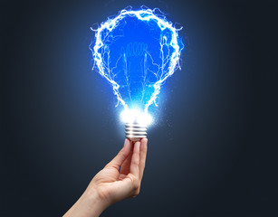 Hand holding shiny light bulb on dark background. New idea concept