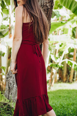 stylish young attractive woman dressed in a light sexy red dress photographed in the summer on a background of palm trees and the sea in the bright sun