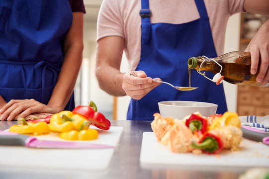 Male And Female Adult Students Adding Olive Oil To  Dish In Kitchen Cookery Class