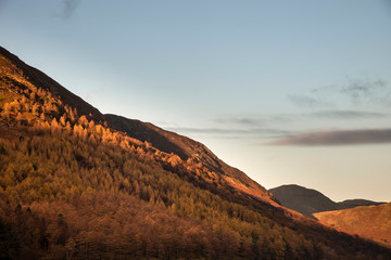 Majestic vibrant Autumn Fall landscape Buttermere in Lake District with beautiful early morning sunlight playing across the hills and mountains