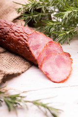 Krakowska dried sausage cut onto slices on wood boards decorated with jute fabric and rosemary. Traditional cold cuts.