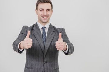 Handsome businessman standing, giving thumbs up, smiling, showing his satisfaction. Focus on the thumbs on the forefront.