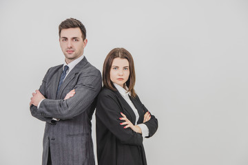 Business man and woman standing alongside, looking confidently at the camera, their hands folded.