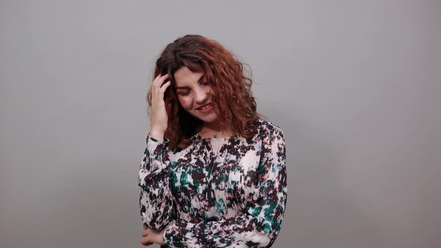 Beautiful charming young lady over isolated gray background in fashion shirt pointing finger on muth, keeping hand on head, holding eyes closed, relaxing. People emotions. Lifestyle concept